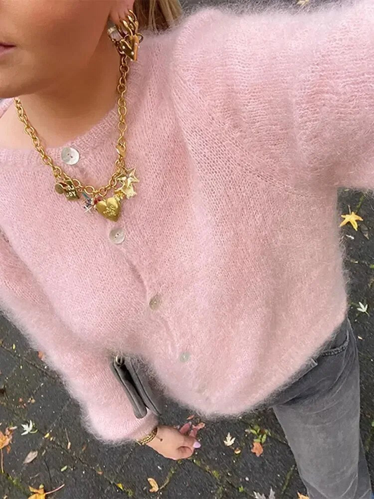 Frau trägt rosa Vintage-Plüsch-Wollstrickjacke, goldene Halskette, graue Jeans.