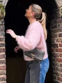 Frau in rosa Strickjacke aus Plüschwolle, graue Umhängetasche, Jeans, vor Backsteinbogen.