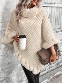 Frau in cremefarbenem Strickponcho mit Kaffeetasse und Handtasche vor Holztor.