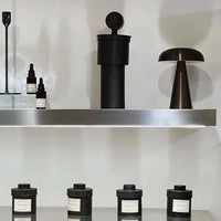Moderne schwarze Duftkerzen und Aromaflaschen auf Metallregal, minimalistische Dekoration.