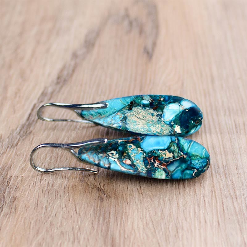 Blaue Tropfen-Ohrringe aus Naturstein auf Holzoberfläche, handgefertigter Schmuck.