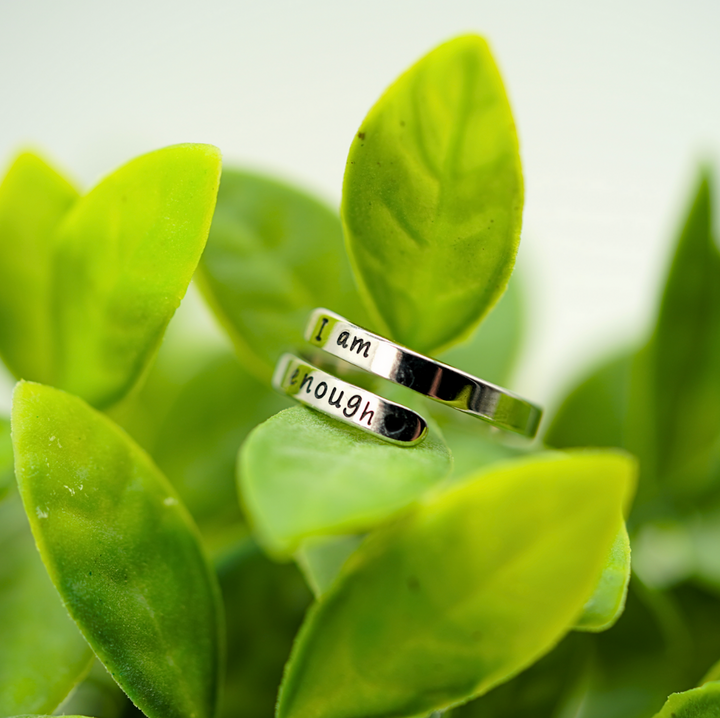 Silberner Motivationsring "I am enough" auf grünen Blättern, Schmuck, Selbstliebe, Geschenkidee.