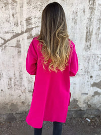 Frau in pinkem, halblangem Kapuzenmantel vor Betonwand, modische Damenjacke.