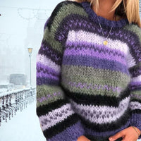 Frau in gestreiftem, mehrfarbigem Strickpullover vor verschneiter Stadtlandschaft.
