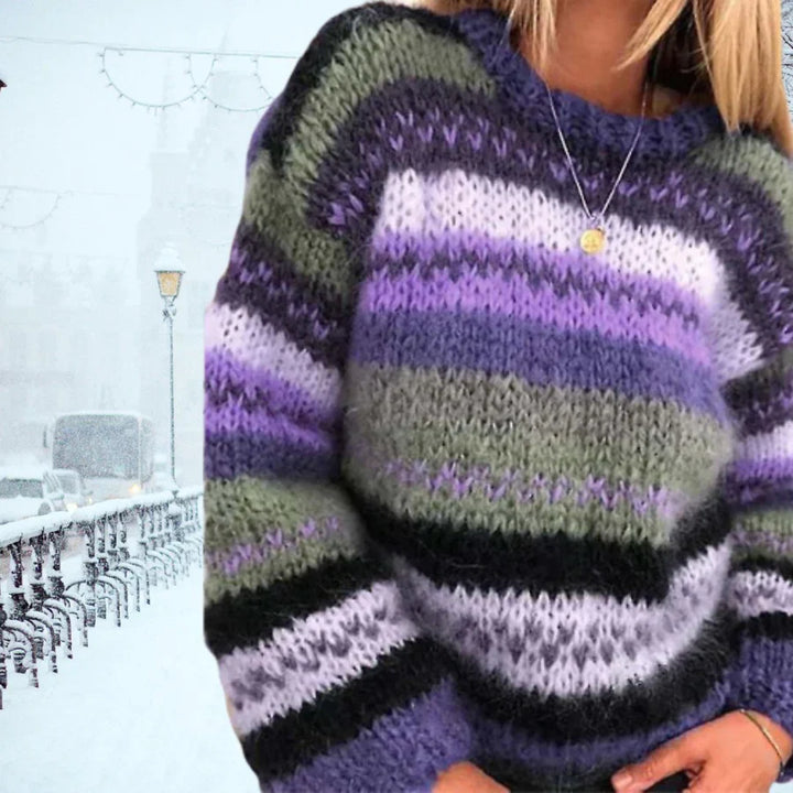 Frau in gestreiftem, mehrfarbigem Strickpullover vor verschneiter Stadtlandschaft.