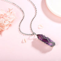 Silberkette mit lila Edelstein-Anhänger, filigranes Design, auf rosa Hintergrund.