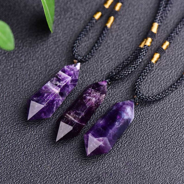 Drei Amethyst-Anhänger an schwarzen Ketten auf schwarzem Hintergrund, Edelstein-Schmuck.