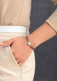 Frau trägt handgemachtes Amethyst-Opal-Yoga-Armband, Boho-Stil, lila, auf beigem Hintergrund.