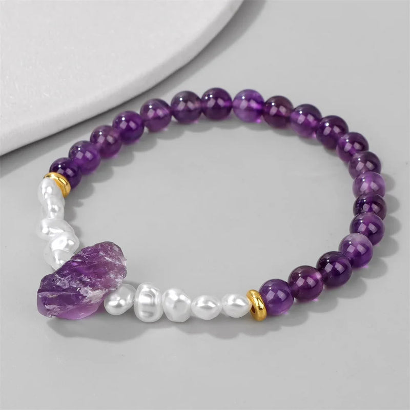 Amethyst-Armband mit weißen Perlen, lila Edelsteinen und goldenen Akzenten auf grauem Hintergrund.