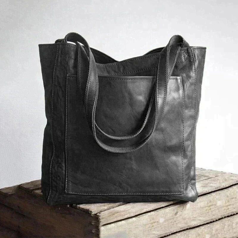 Schwarze Ledertasche, langlebig, modisch, robust, für Damen, auf Holzkiste.