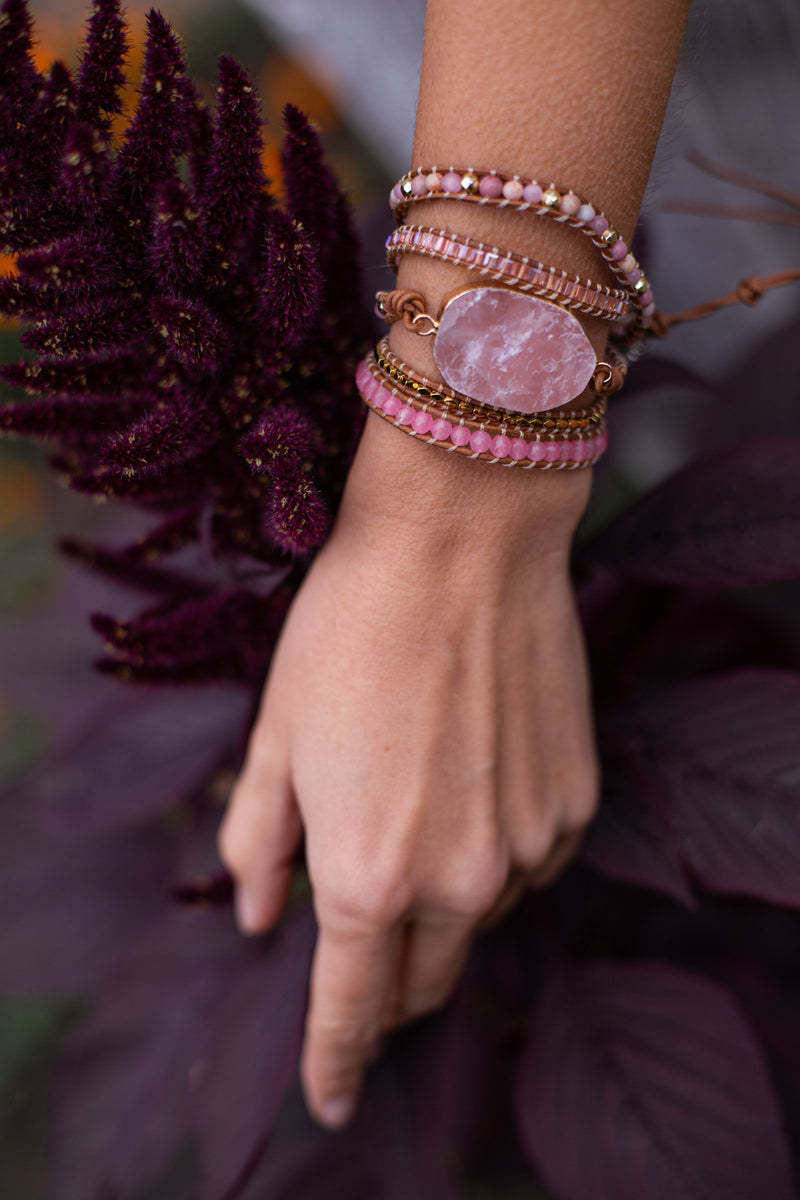 Armband mit rosa Kristall, handgefertigt, Boho-Stil, an Arm mit lila Blumen im Hintergrund.