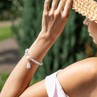 Frau mit weißem Perlenarmband und Tropfenanhänger, Sommerhut, Naturhintergrund.