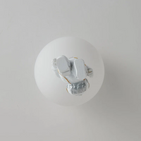 Weiße Glaskugel mit silberner Astronautenfigur, moderne Dekoration, minimalistisches Design.