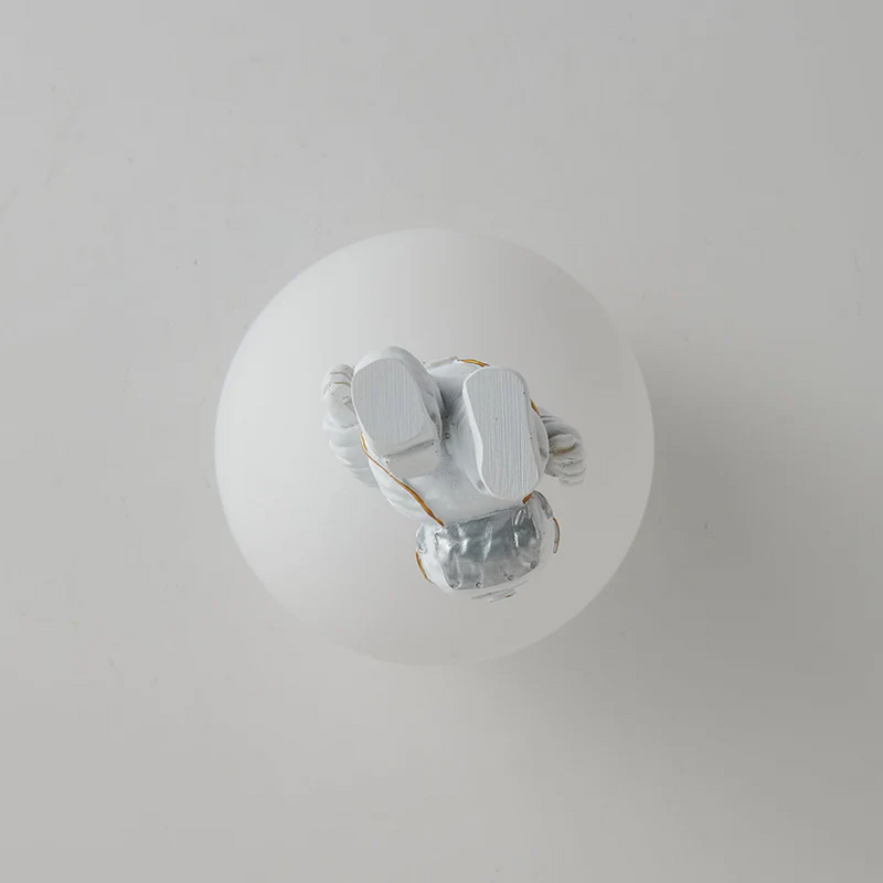 Weiße Glaskugel mit silberner Astronautenfigur, moderne Dekoration, minimalistisches Design.