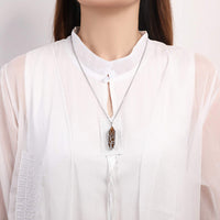 Frau mit weißer Bluse und silberner Halskette mit braunem Blattanhänger, eleganter Schmuck.