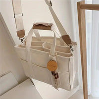 Beige Canvas Handtasche mit Schulterriemen, Organizer-Fächern und Schlüsselanhänger.