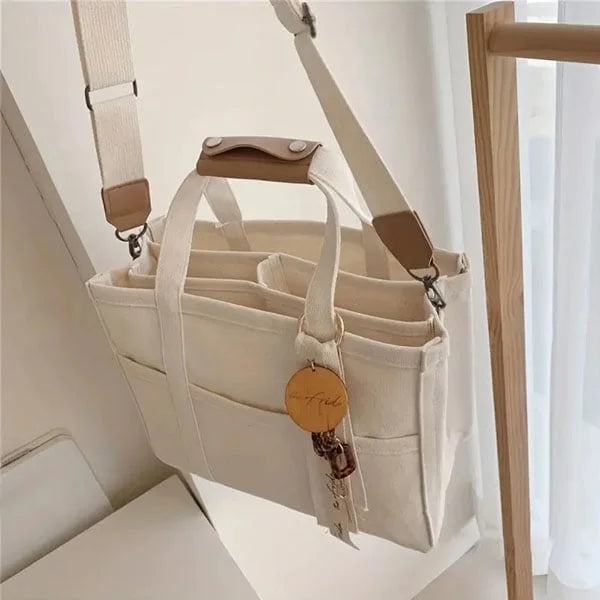 Beige Canvas Handtasche mit Schulterriemen, Organizer-Fächern und Schlüsselanhänger.