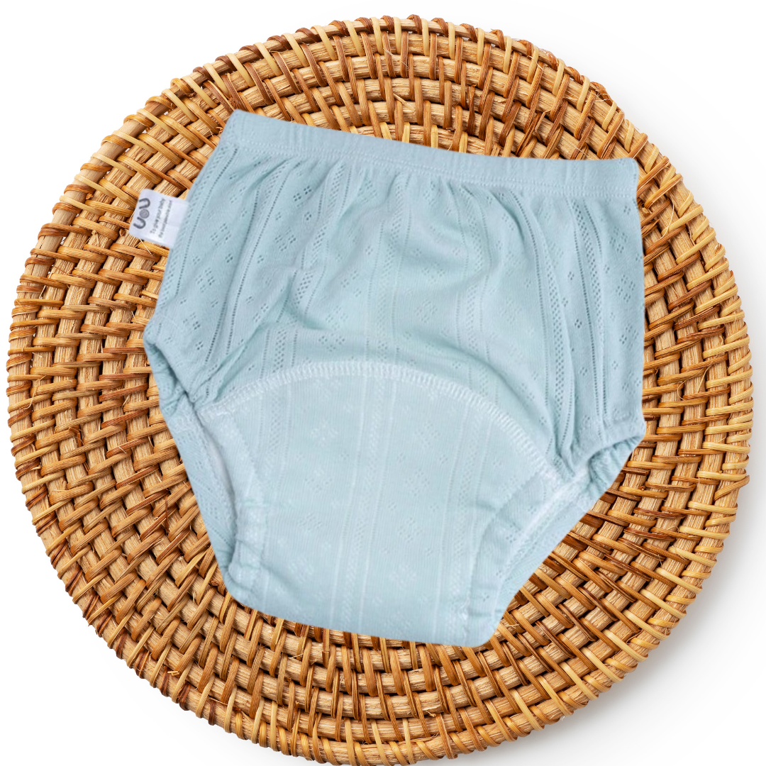 Hellblaue Babyunterhose aus Baumwolle auf rundem, geflochtenem Korb.
