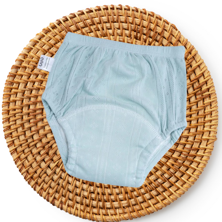 Hellblaue Babyunterhose aus Baumwolle auf rundem, geflochtenem Korb.