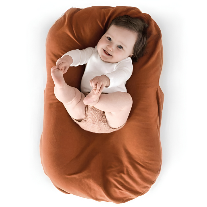 Lächelndes Baby auf braunem Kissen, weißer Body, Babyfotografie, gemütlich, niedlich.