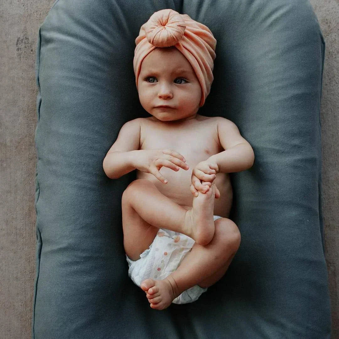 Kleinkind mit rosa Turban auf grauem Babynest, Babyfotografie, Neugeborenenmode.