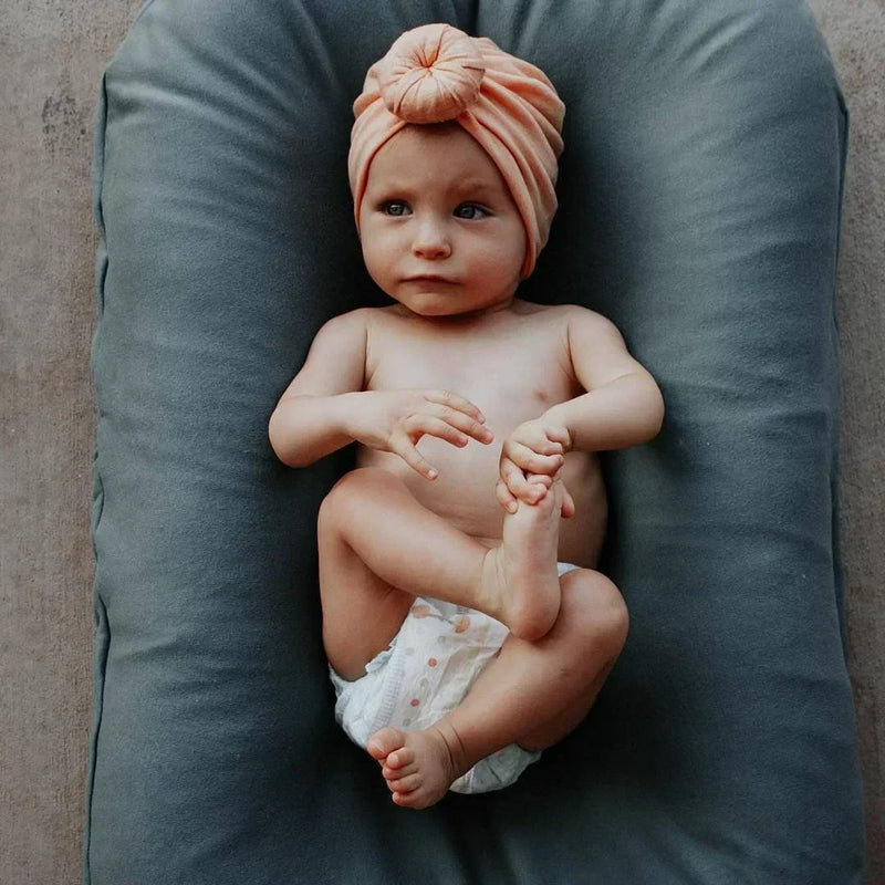 Kleinkind mit rosa Turban auf grauem Babynest, Babyfotografie, Neugeborenenmode.