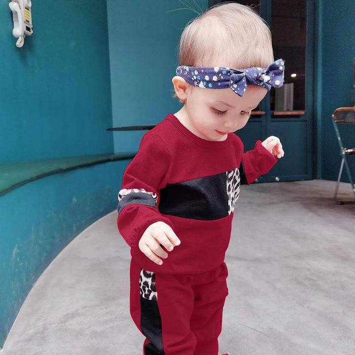 Kleinkind in rotem Trainingsanzug mit Leopardenmuster und blauem Stirnband in modernem Raum.