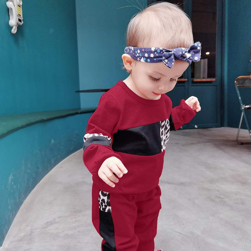 Kleinkind in rotem Trainingsanzug mit Leopardenmuster und blauem Stirnband in modernem Raum.