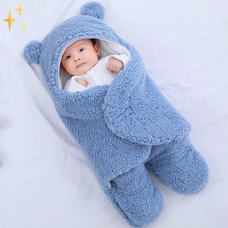 Baby in blauem Plüsch-Babysack mit Bärenohren, weich und warm, ideal für Neugeborene.