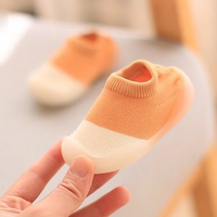 Orange-weiße Babyschuhe aus Baumwolle, rutschfest, handgehalten, auf grauem Hintergrund.