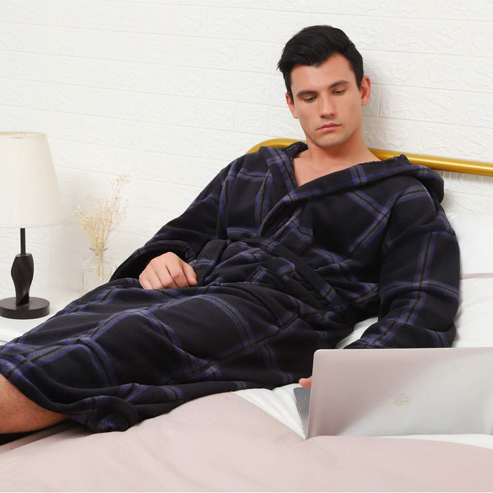 Mann im schwarzen karierten Fleece-Bademantel auf Bett mit Laptop, gemütliche Heimkleidung.