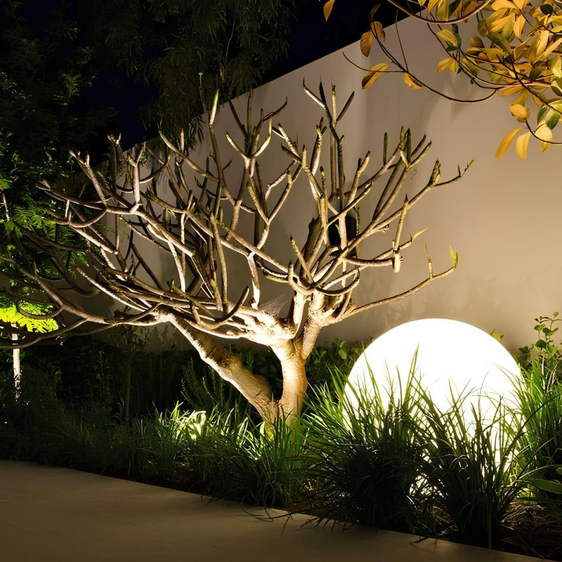 Beleuchteter Garten mit Baum und großer, runder Lampe bei Nacht, moderne Außenbeleuchtung.