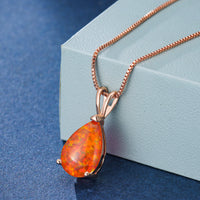 Opal-Anhänger in Tropfenform mit roségoldener Kette auf blauem Hintergrund.