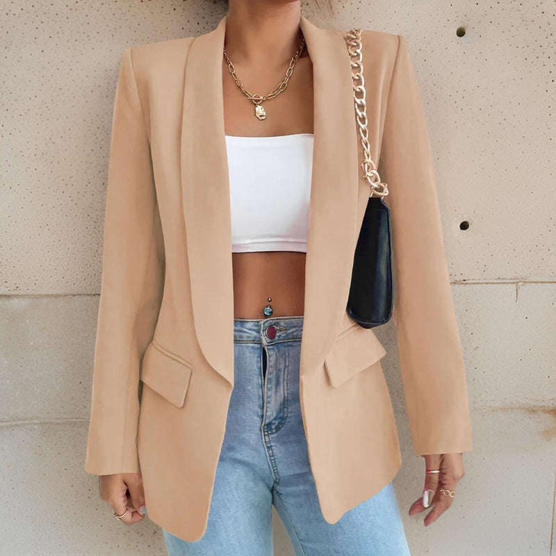 Frau in beigem Blazer, weißem Top, blauer Jeans, schwarze Tasche, modisch, elegant.