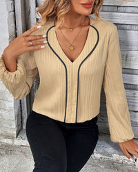 Frau in beige Bluse mit schwarzem Rand, V-Ausschnitt, lange Ärmel, modisch, elegant.