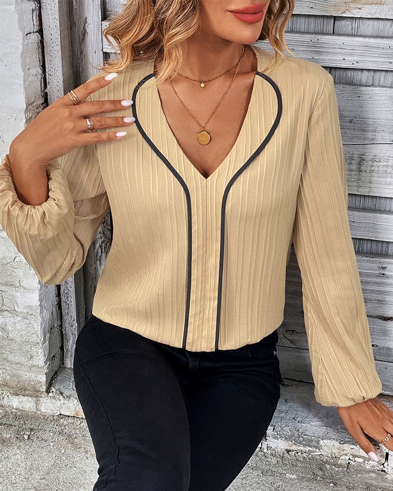 Frau in beige Bluse mit schwarzem Rand, V-Ausschnitt, lange Ärmel, modisch, elegant.