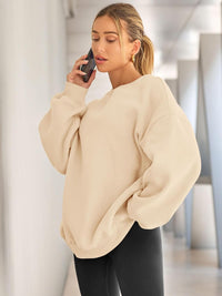 Frau in beigem Oversize-Pullover, telefonierend, moderne Mode, gemütlicher Look, Innenraum.