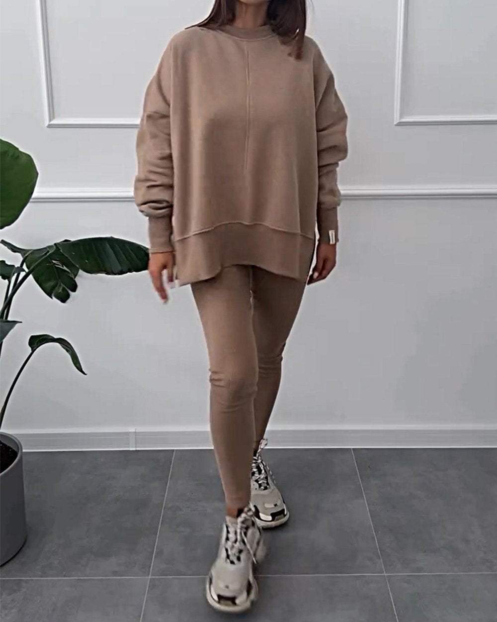 Frau in beigem Oversize-Sweatshirt und Leggings, modisch, lässig, Indoor, Pflanzenhintergrund.