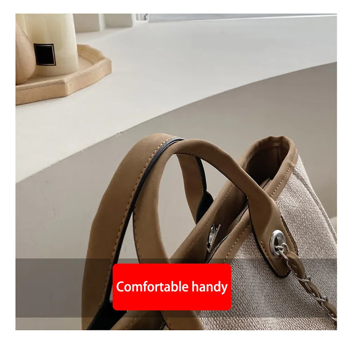 Beigefarbene Handtasche aus Stoff mit braunen Ledergriffen auf einem Tisch.