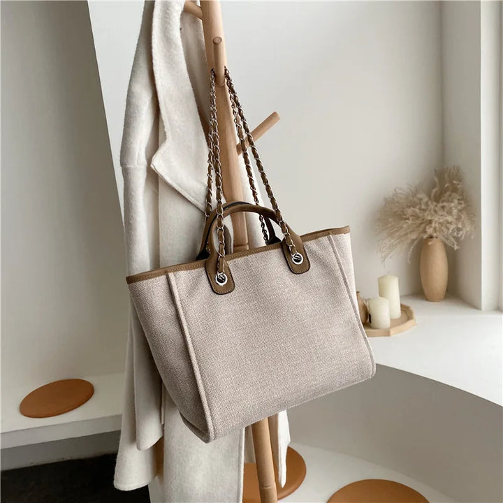 Beige Damenhandtasche aus Leinen mit braunen Ledergriffen, hängend an Holzständer.