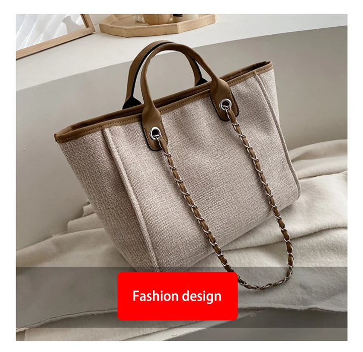 Beige Damenhandtasche aus Leinen mit braunen Ledergriffen und Kettendetail.