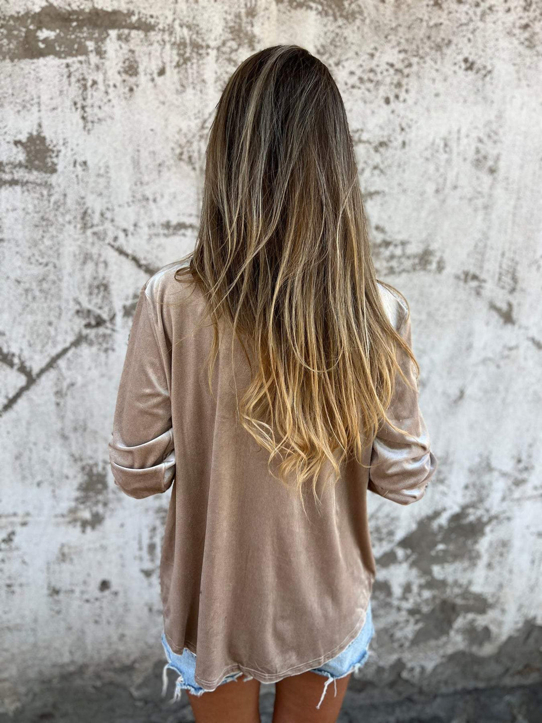 Frau mit langen Haaren in beigem Samtoberteil vor Betonwand, modisch, lässig, Streetstyle.