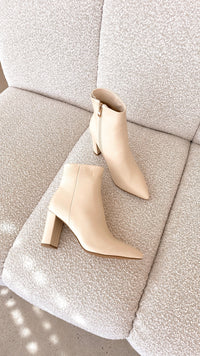 Beige Damen-Stiefeletten mit Blockabsatz auf cremefarbenem Sofa, elegantes Design, Lederoptik.