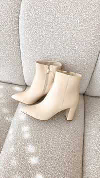 Beige Damenstiefeletten mit Blockabsatz, Reißverschluss, auf beigem Sofa, elegantes Design.