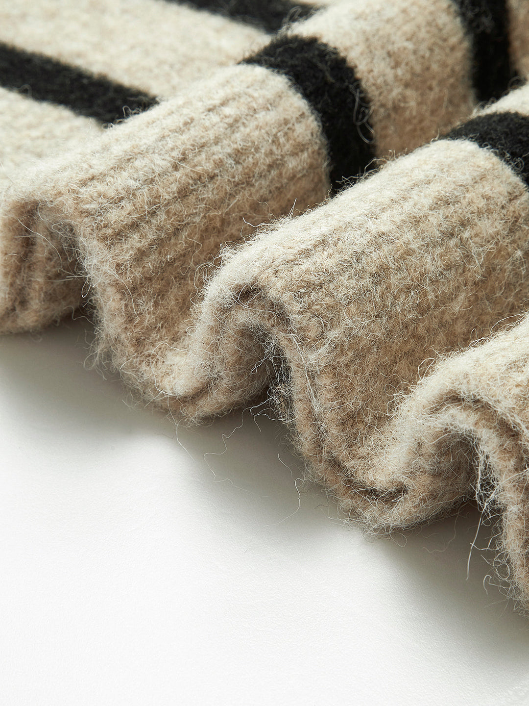 Beigefarbener Wollpullover mit schwarzen Streifen, Nahaufnahme, weiches Material, modisch.