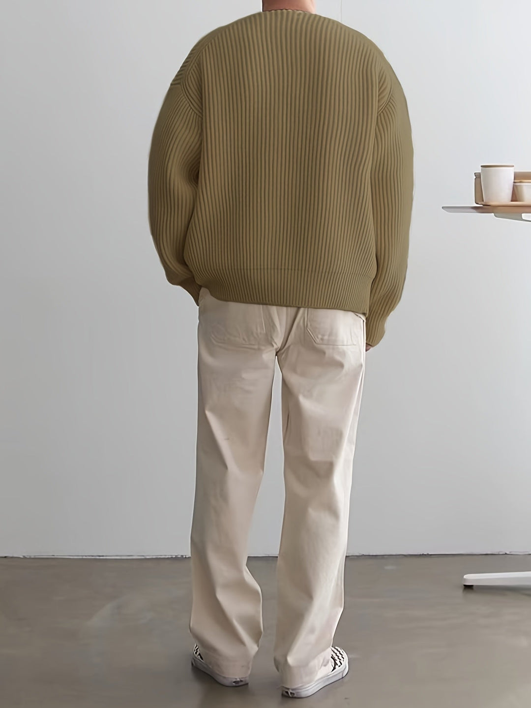 Mann in beigem Strickpullover und weißen Hosen, Rückansicht, moderne Mode, minimalistisch.