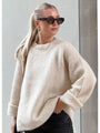 Frau mit beigem Pullover, Sonnenbrille und blonden Haaren in Pferdeschwanz, modisch gekleidet.