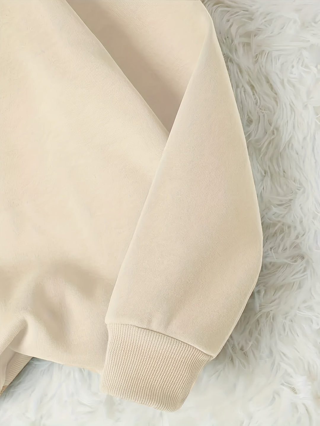 Beiger Pulloverärmel aus Baumwolle auf weißem Fellteppich, modisch, gemütlich, Herbstmode.