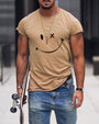 Mann in beigem T-Shirt mit Smiley-Design, Jeans, Skateboard, urbaner Hintergrund.