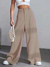 Frau in beigen, weiten Hosen, weißem Top, hält weiße Handtasche, modisch, elegant.